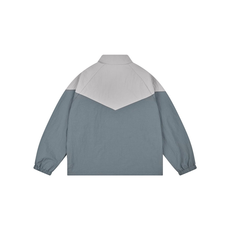 Back view of a slate blue jacket with a light gray chevron-shaped shoulder panel and elastic cuffs.