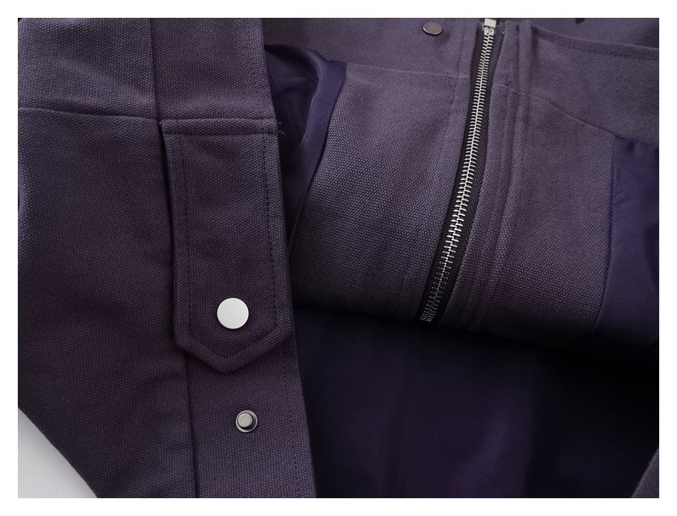 Close-up of a dark plum jacket showing its snap placket, metal zipper, pocket, and dark lining.
