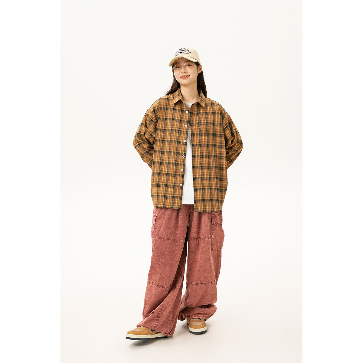 Model wearing an oversized mustard and brown plaid button-up shirt with dusty rose cargo pants.