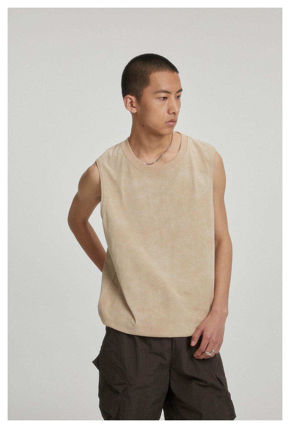 Model wearing a beige sleeveless crewneck top, shown at an angle with dark cargo shorts.