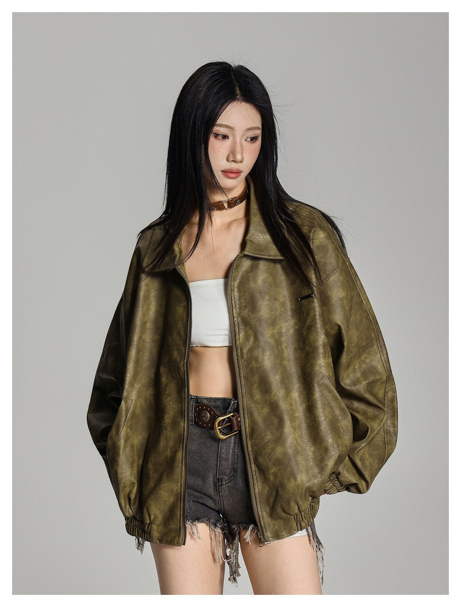 Close view of a model in an olive green snake-textured zip jacket worn open over a white top and denim shorts