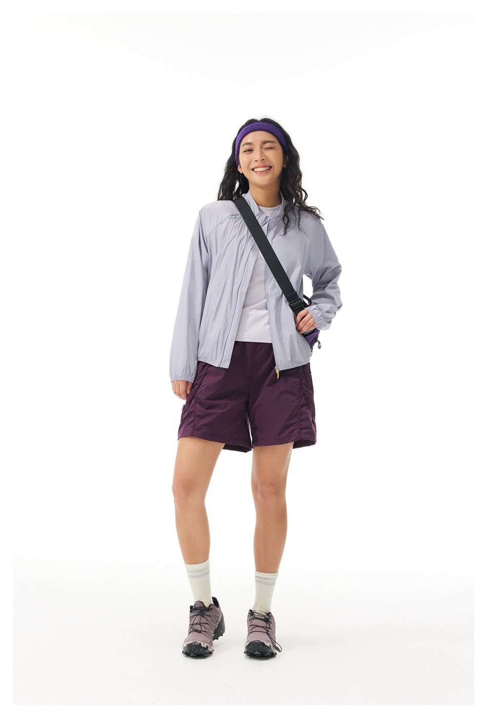 Model wearing an open light lavender jacket over a white top with plum shorts and a crossbody bag.