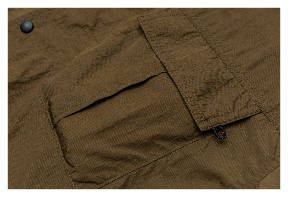 Close-up of an olive-brown jacket pocket with a flap, black snap button, and narrow tab with a loop.