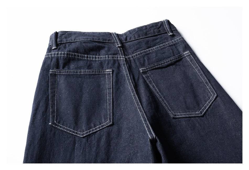Close view of dark indigo jeans from the back, showing two white-stitched pockets and belt loops.