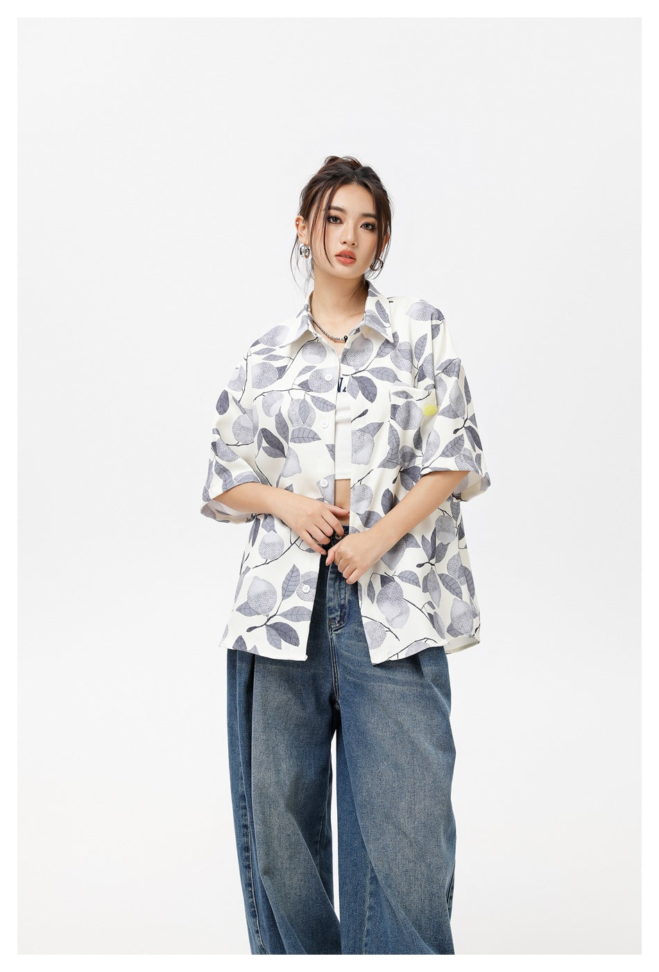 Model wearing an open ivory short-sleeve shirt with a gray botanical print and wide-leg blue jeans.