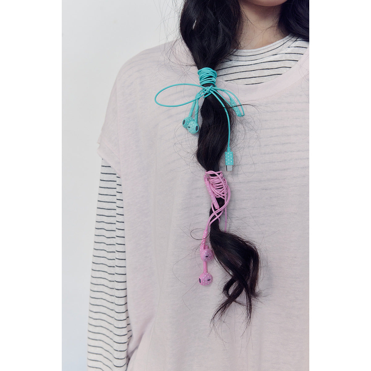 Close-up of a pale pink top layered over a striped shirt, with turquoise and pink cords tied around the model's hair.