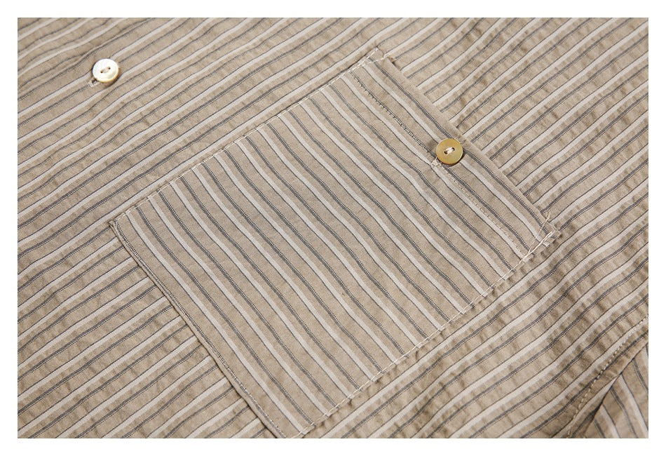 Close-up of a tan shirt with narrow dark stripes, a chest pocket, and light-colored buttons.