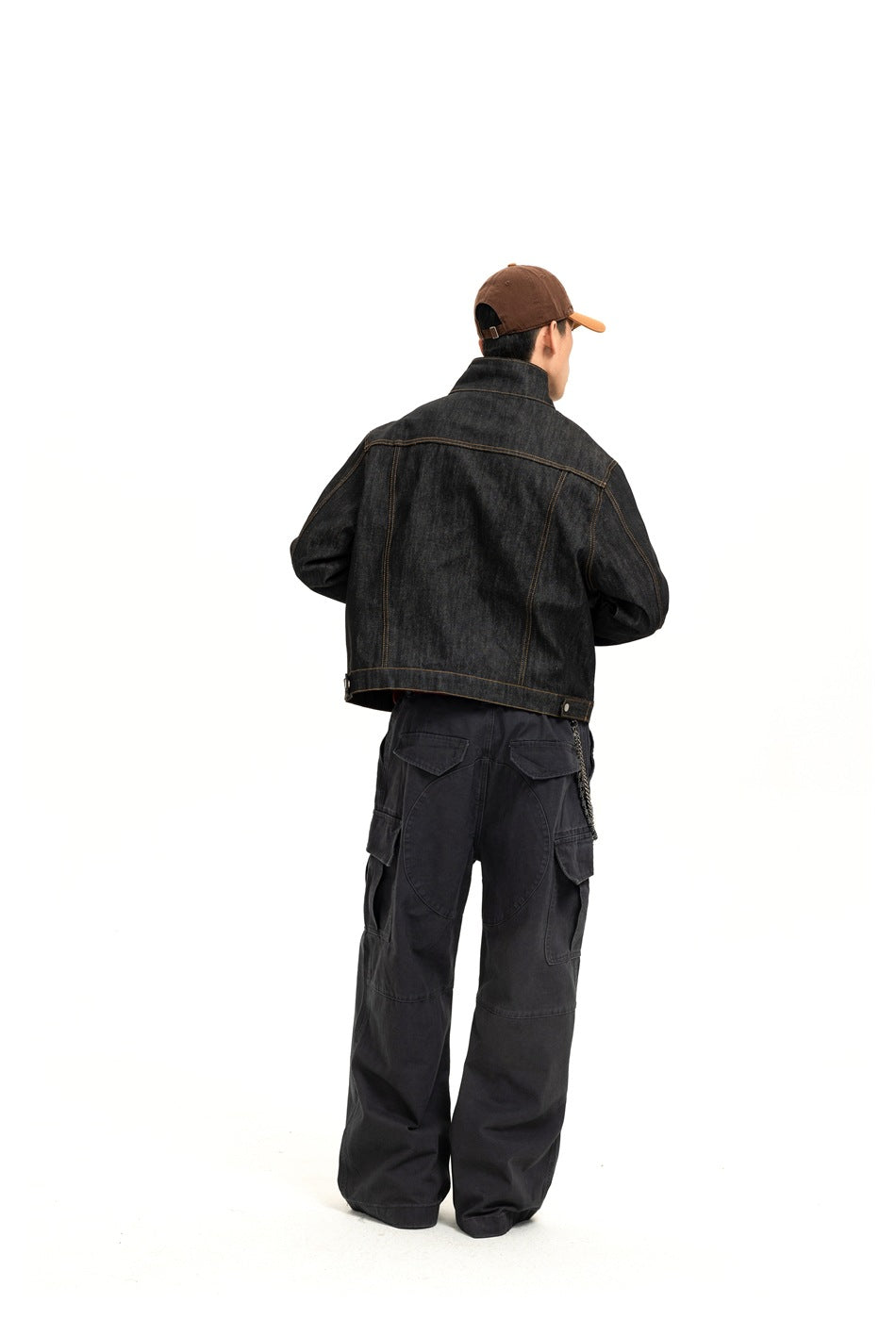 Back view of a model wearing dark gray cargo pants with back flap pockets, curved seaming and a wallet chain
