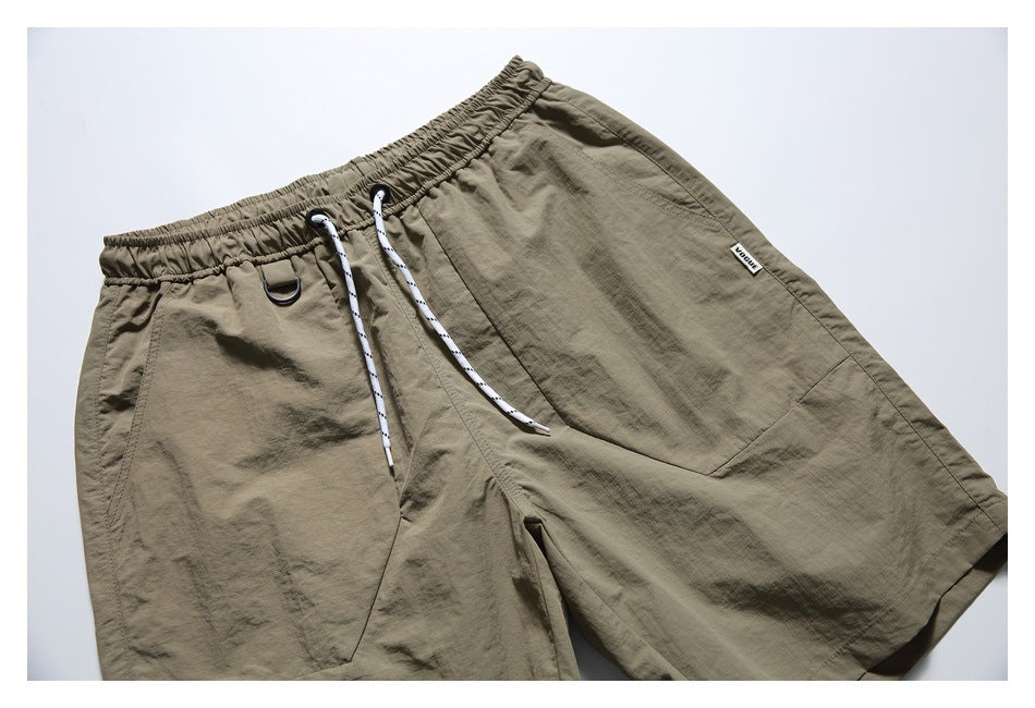 Angled front view of taupe shorts with an elastic drawstring waist, front pockets, and a small sewn label.