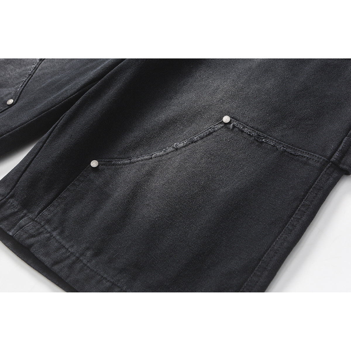 Close-up of a dark shorts leg with a curved pocket seam and small metal rivets.