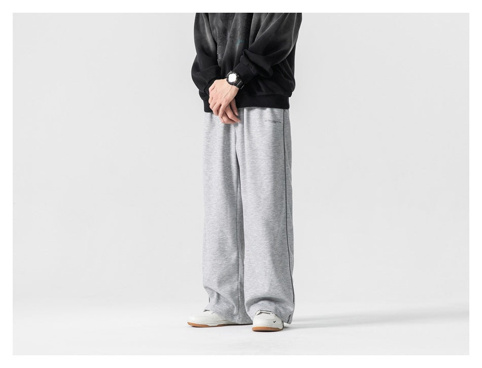 Cropped model wearing loose light gray wide-leg pants with a black sweatshirt and white sneakers, front view.