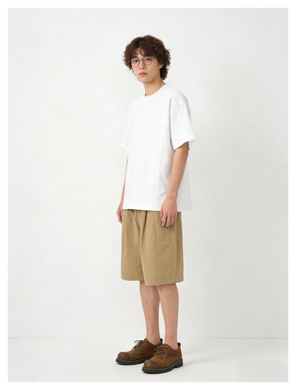 Model wearing a plain oversized white crew-neck T-shirt with short sleeves and tan shorts.