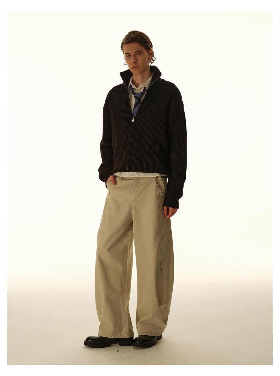 Model wearing a dark ribbed zip-up cardigan over a white shirt and striped tie with loose beige trousers.