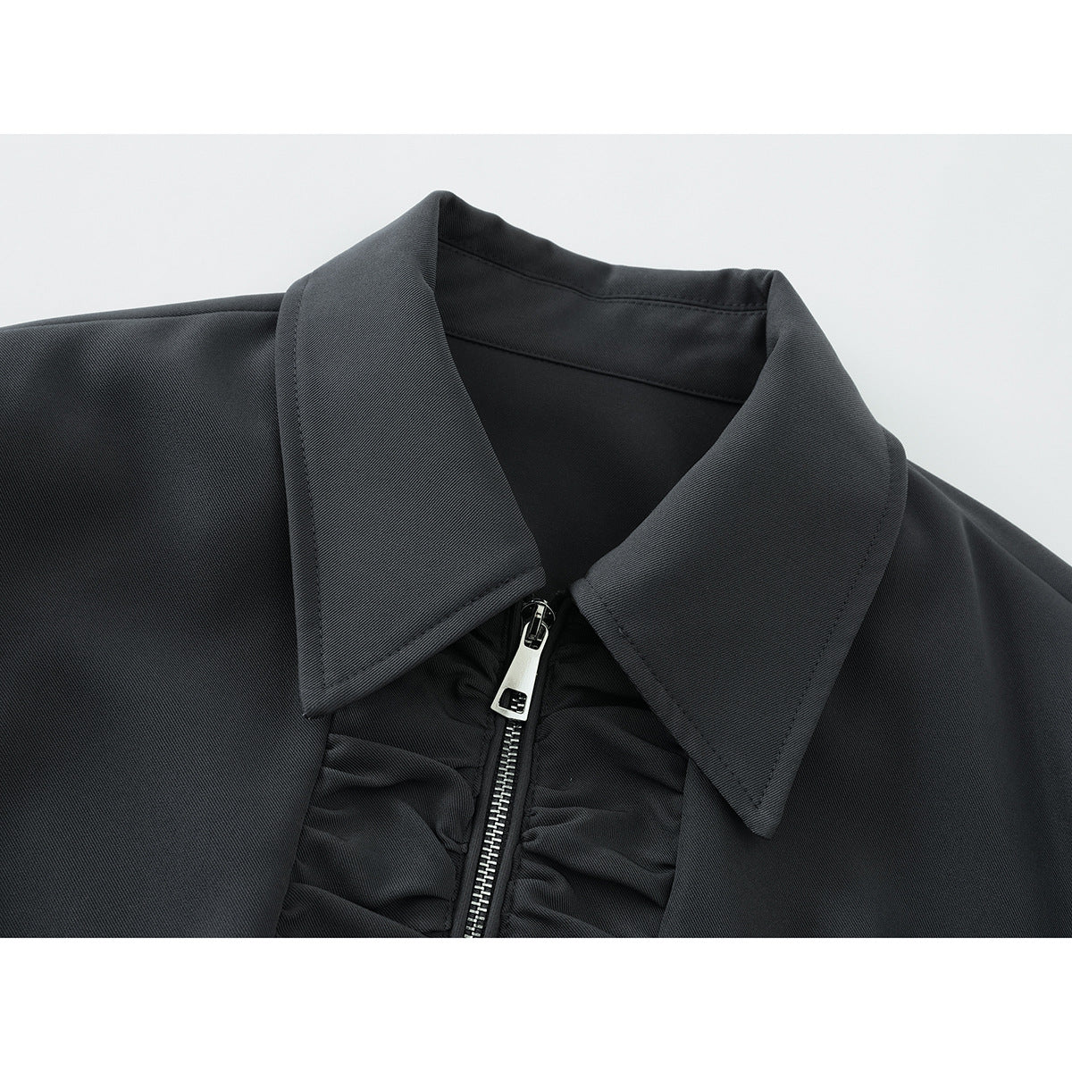 Close-up of a charcoal jacket’s pointed collar and silver front zipper with gathered trim.