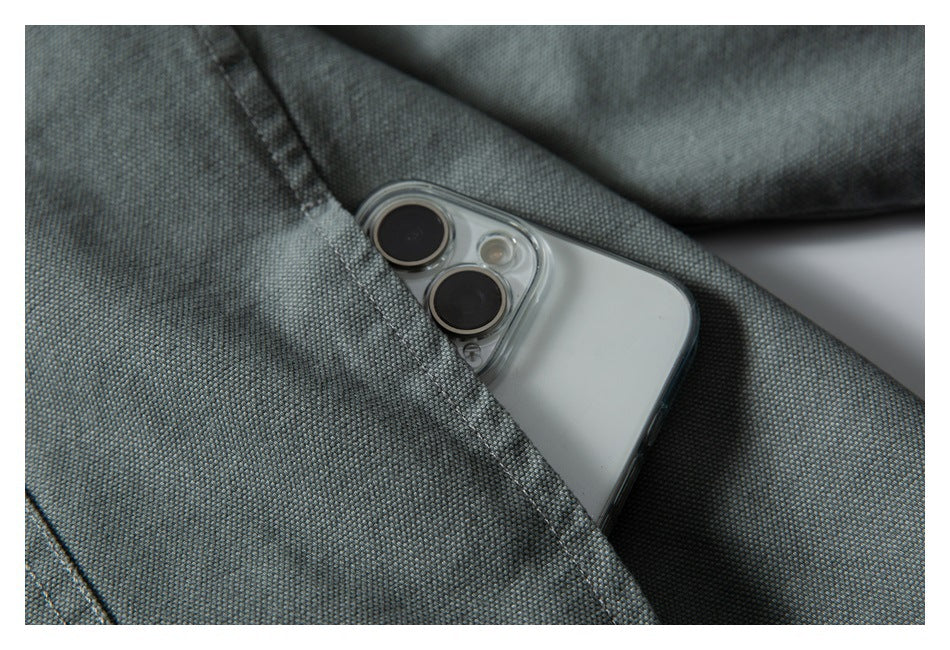 A smartphone tucked into the chest pocket of a gray-green jacket, showing the pocket opening and fabric texture.