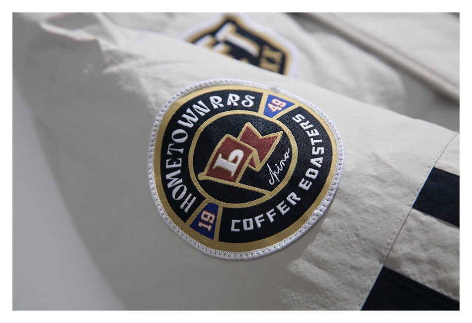 Close-up of a circular black, gold, and white embroidered patch on the off-white jacket sleeve.