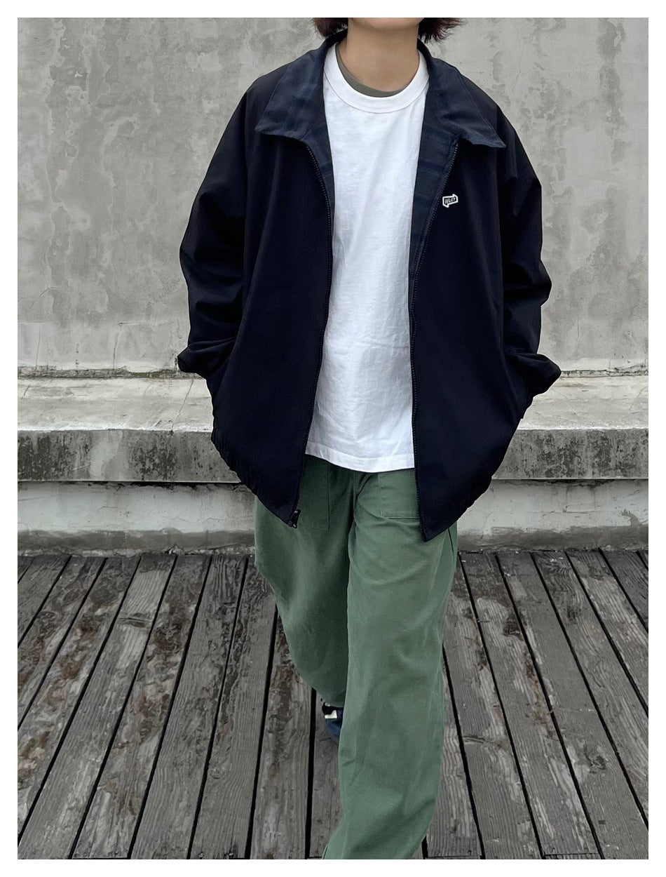 Person wearing a black collared zip jacket over a white T-shirt and green trousers.