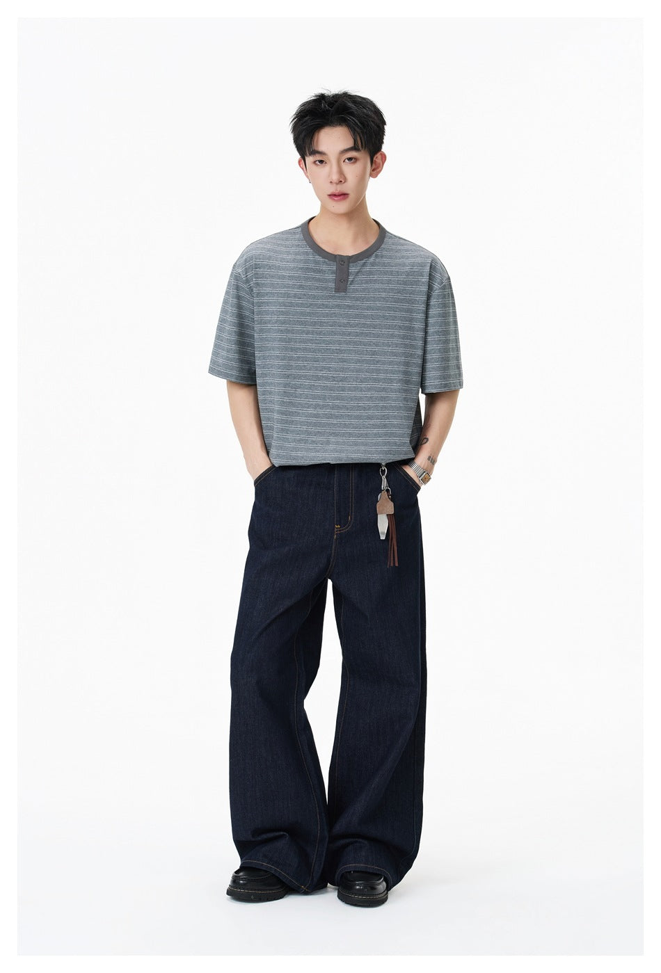 Full-length view of a model wearing a gray striped Henley and loose dark jeans.