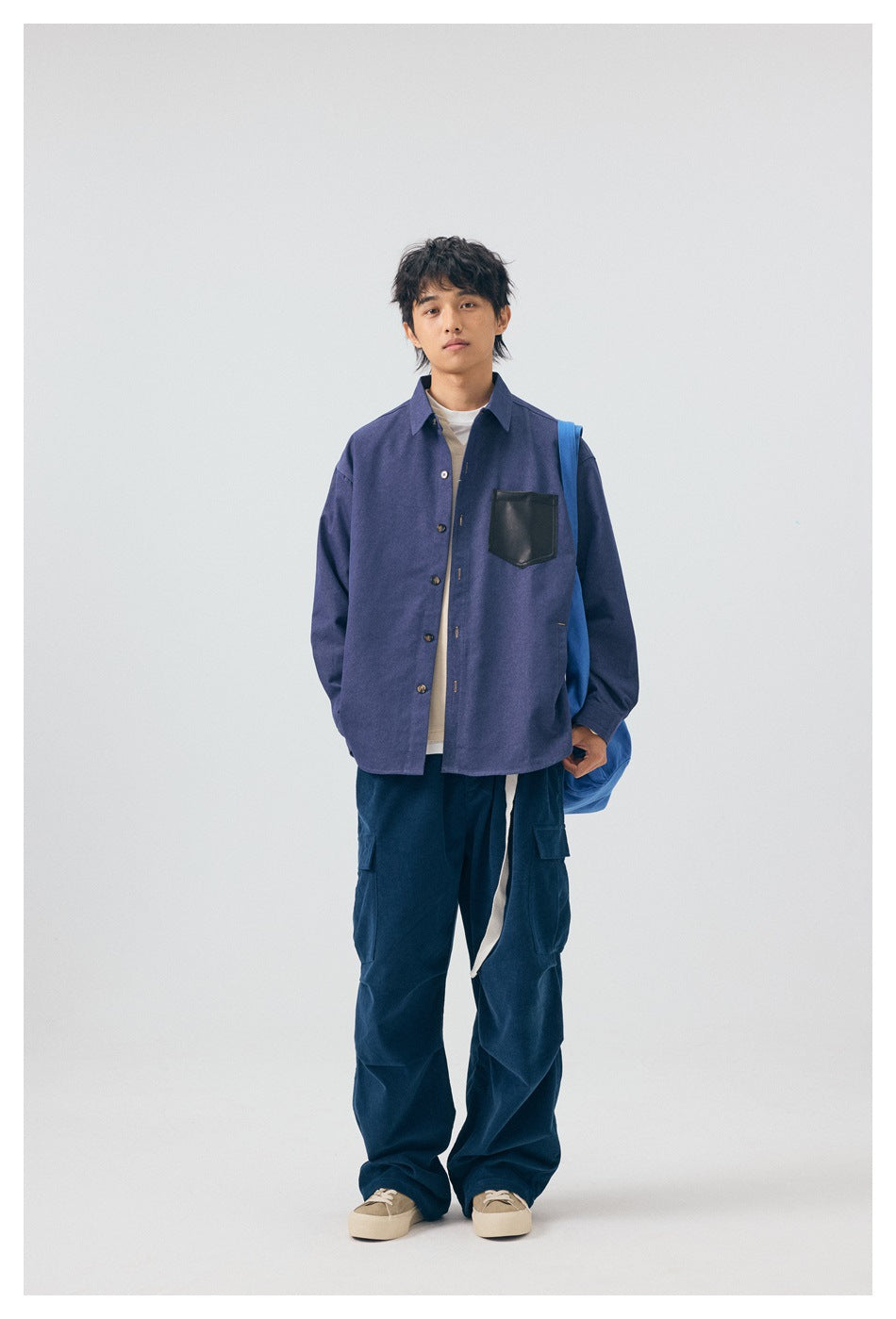 Model wearing a blue button-up shirt with a black chest pocket over a light tee, with navy cargo pants