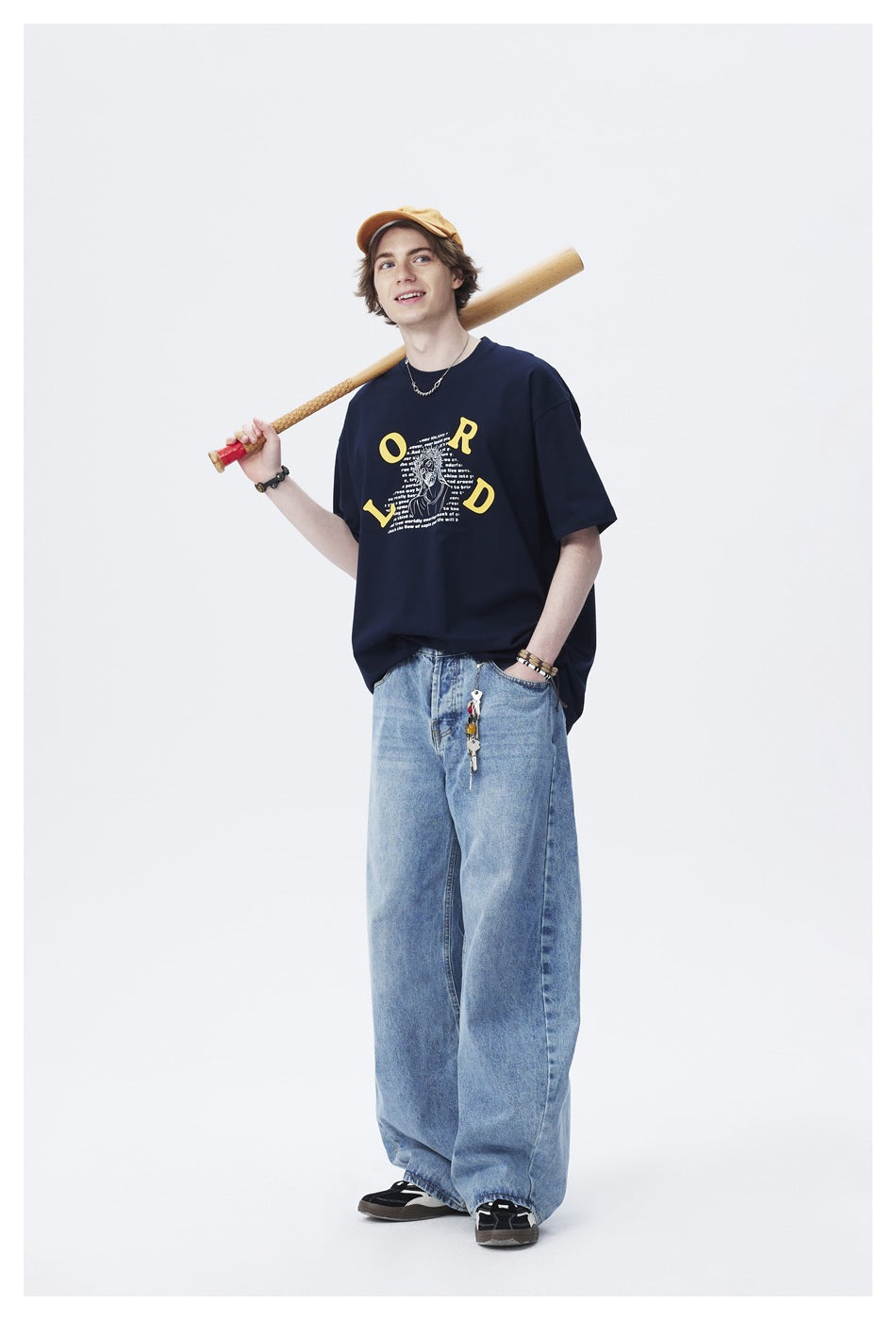 Model wears a navy graphic T-shirt and loose light-blue jeans with a mustard cap.