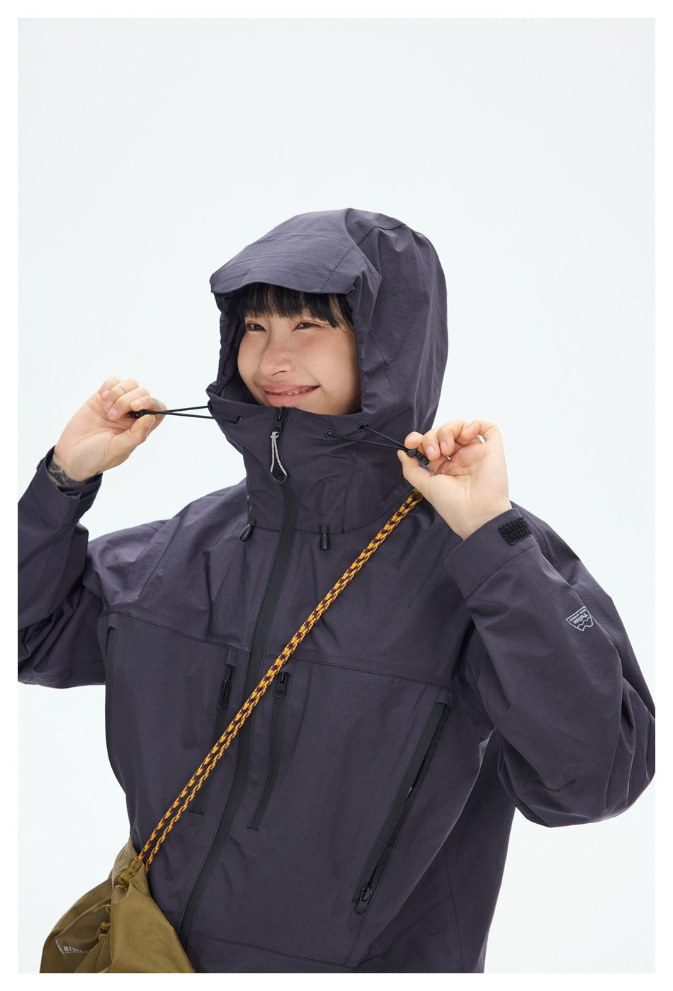 Close-up of a model adjusting the hood cords on a dark plum jacket with multiple zip pockets.