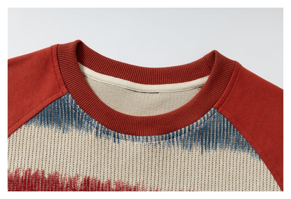 Close-up of a rust-red ribbed crew neck and shoulder seams on a cream knit shirt with blue and red accents.