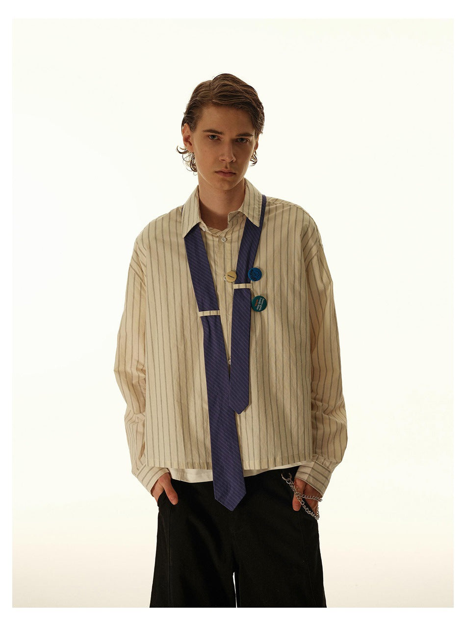 Model in a beige vertically striped shirt with a navy tie and decorative pins, shown from the waist up.