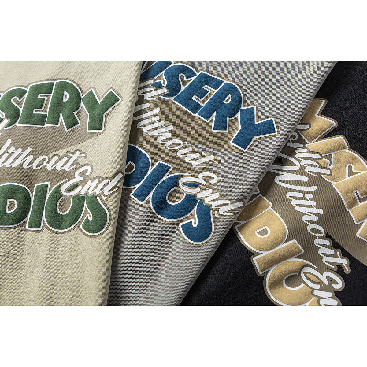 Close-up of three T-shirt colorways with large contrasting “Misery World Without End Studios” chest prints.