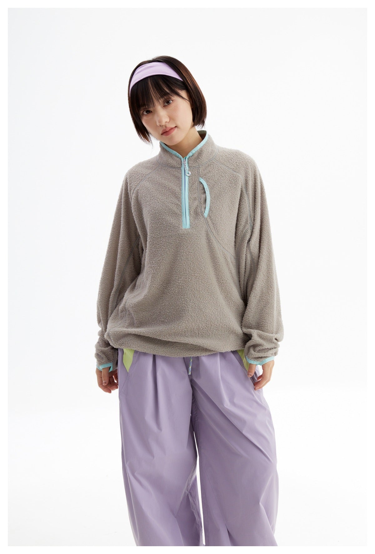 Front view of a model wearing a taupe fleece pullover with aqua trim and lavender pants.