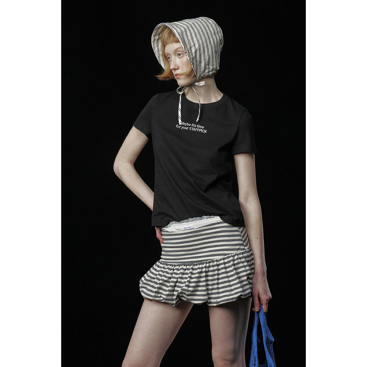 Model wearing a black short-sleeve T-shirt with small English chest text and a gray-and-white striped ruffle skirt.