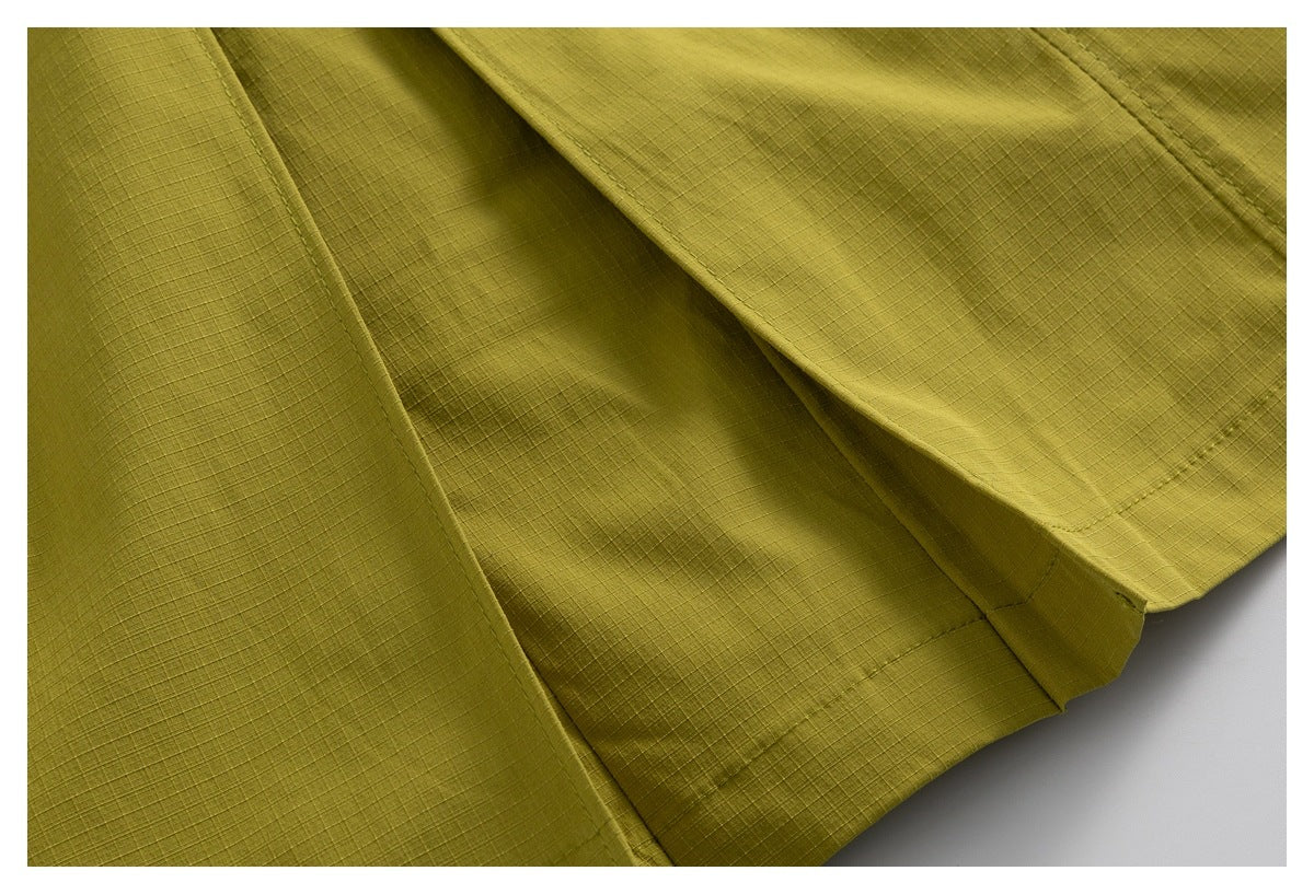 Close-up of olive-yellow shorts showing overlapping fabric panels and stitched seams.