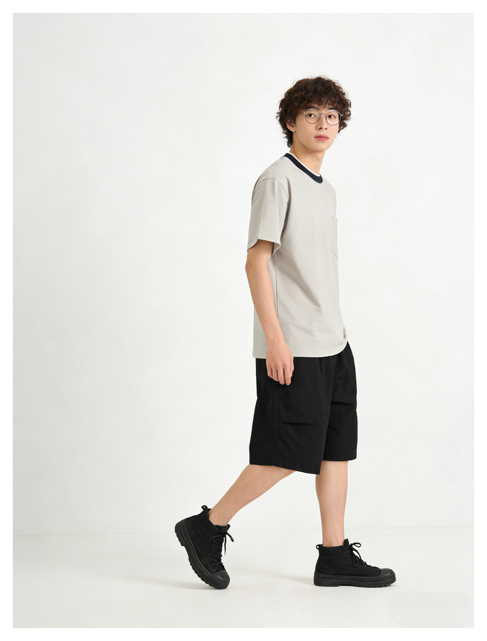 Side view of a model in a light gray pocket T-shirt with a dark contrast collar and black shorts.