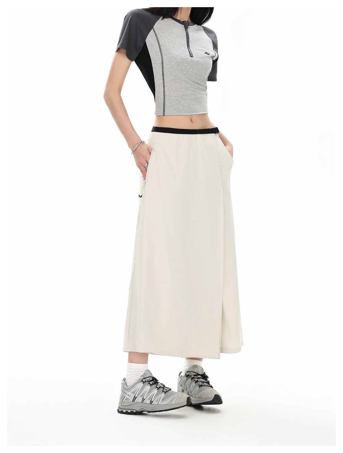 Model wearing a long light beige skirt with a black belt and side pockets, shown from the front.