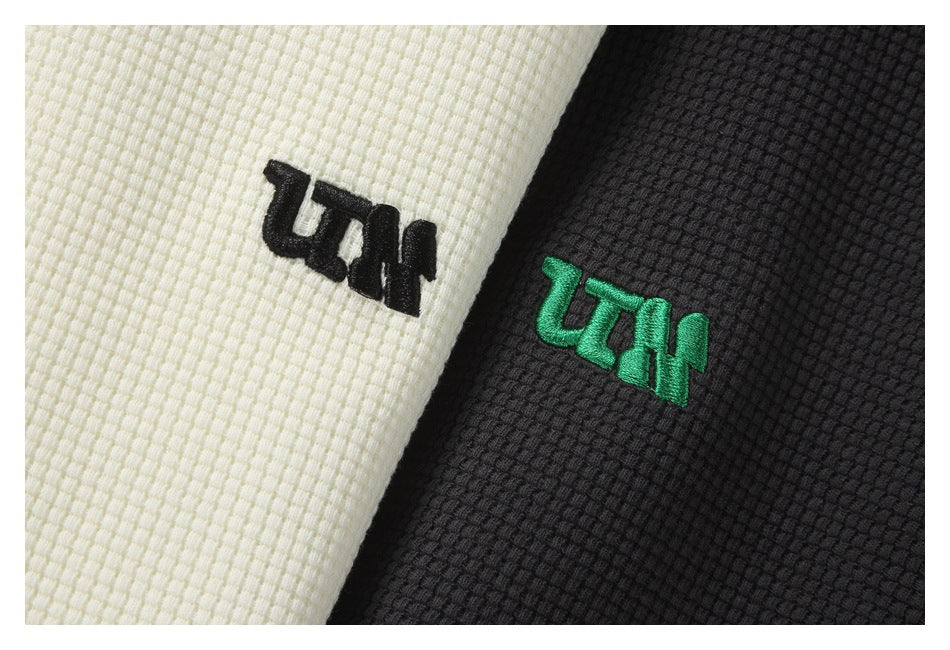Close-up of embroidered symbols on off-white and black textured fabric.