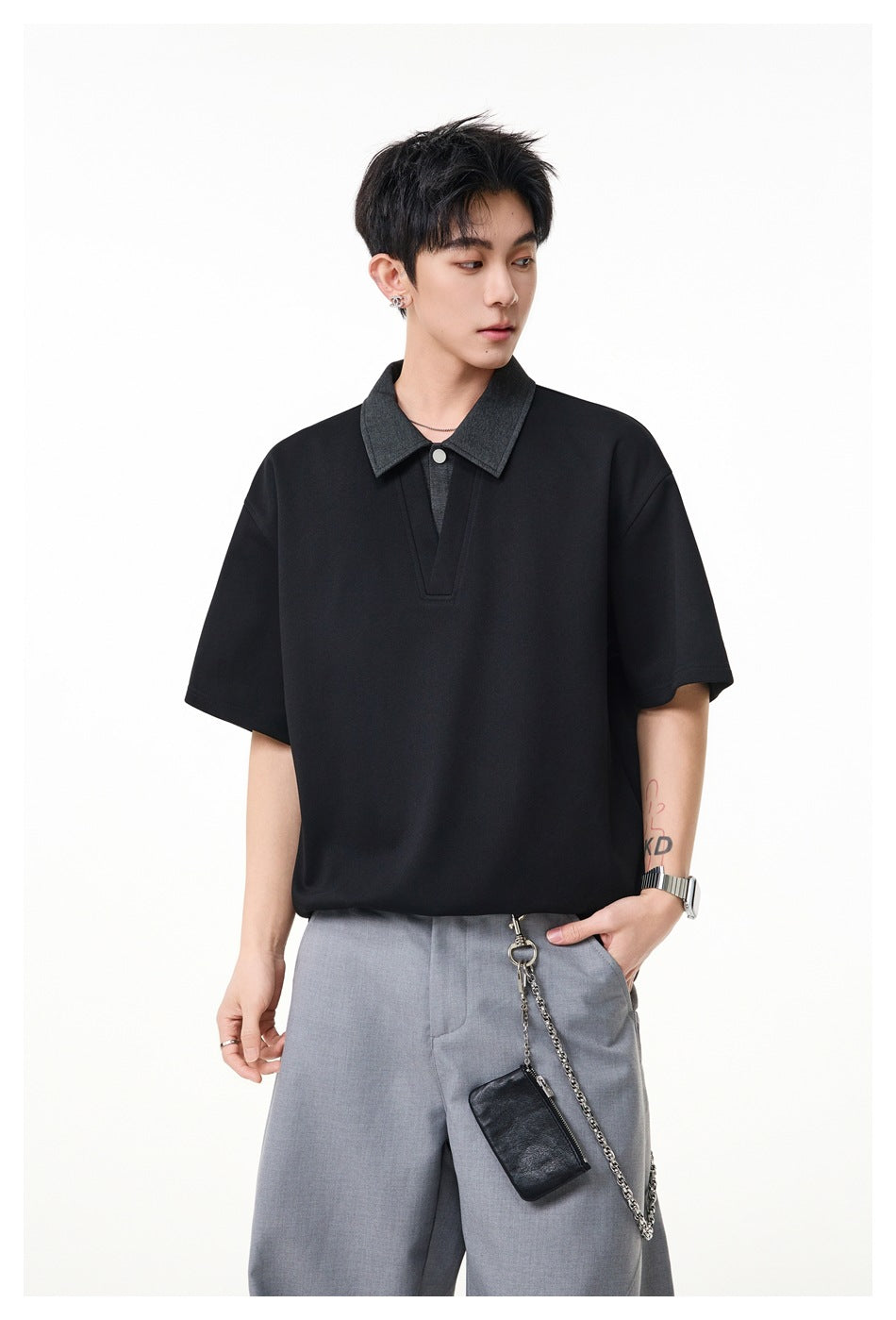 Model wearing black short-sleeve polo top with gray collar, styled with gray trousers and a chain pouch