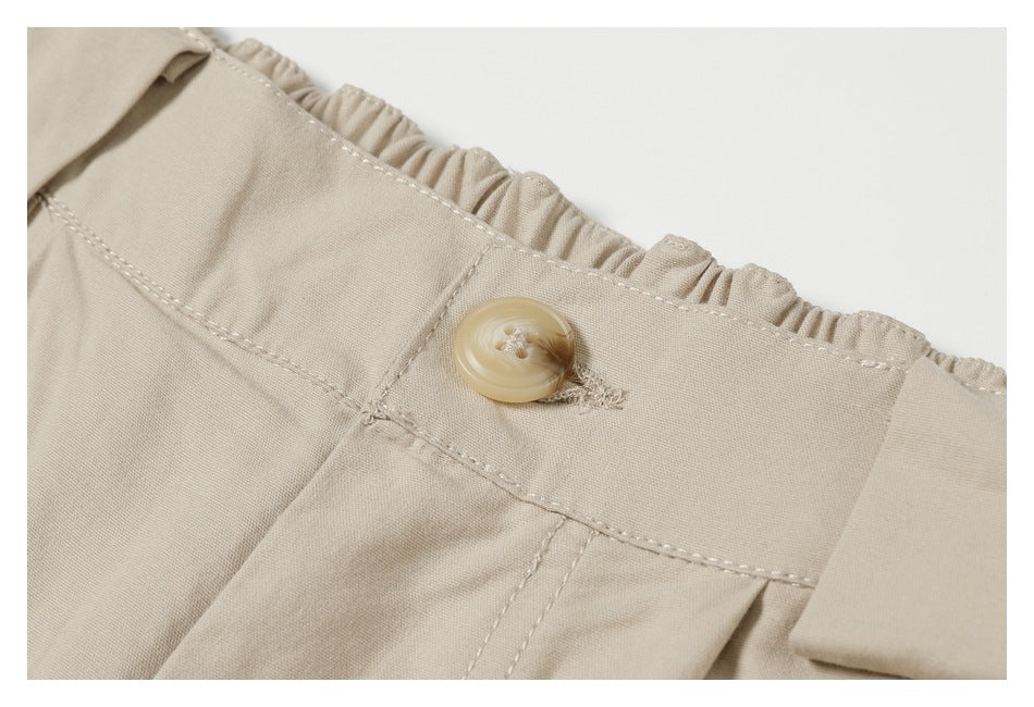 Close-up of beige trousers showing a gathered waistband, button, stitching and belt loop.