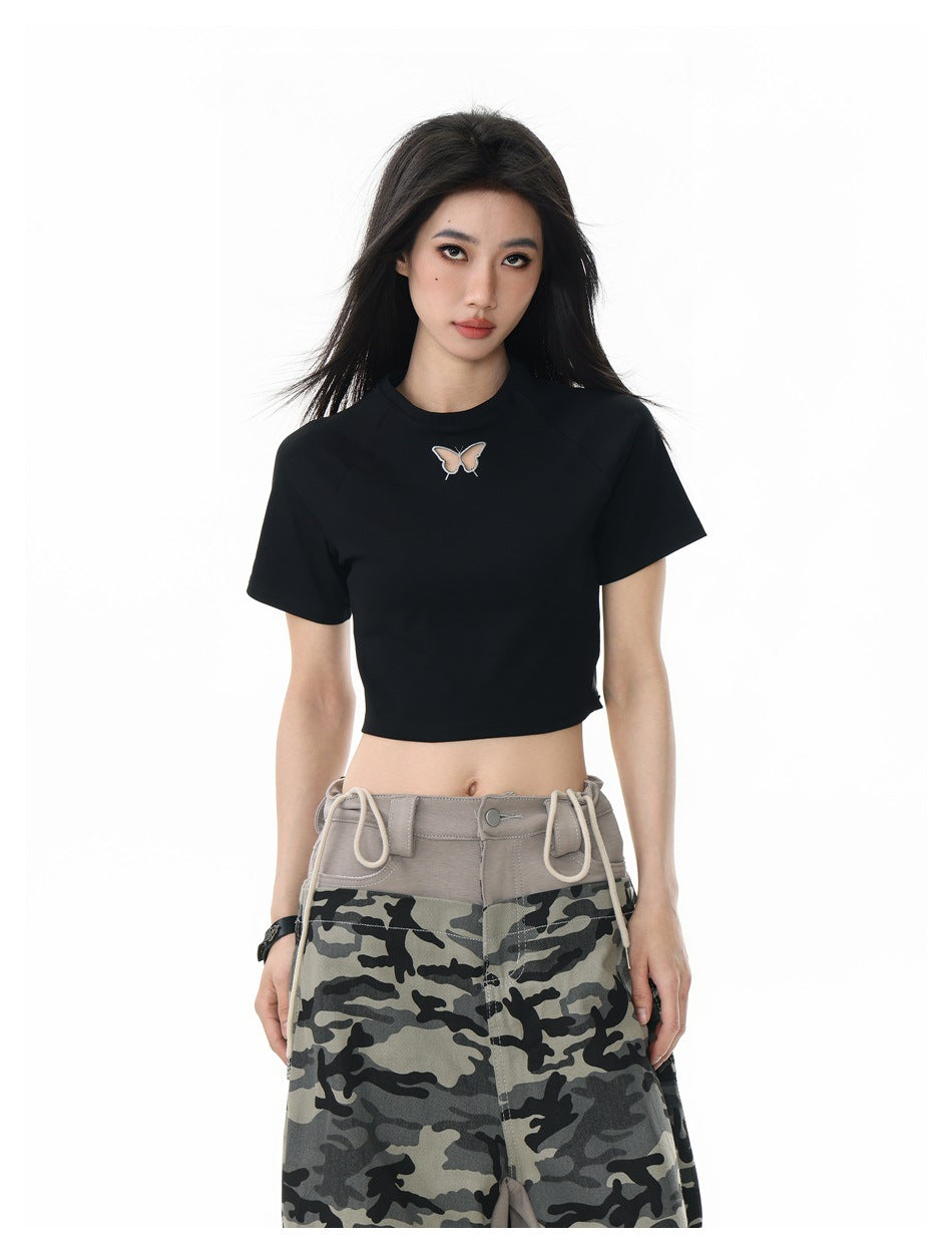 Woman in a black cropped raglan T-shirt with a butterfly motif at the chest, close front view