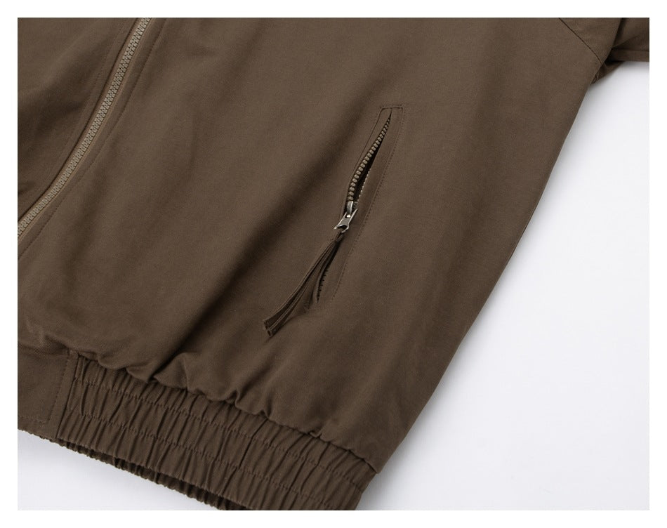 Close-up of a brown jacket showing its front zipper, slanted zip pocket, and gathered elastic hem.