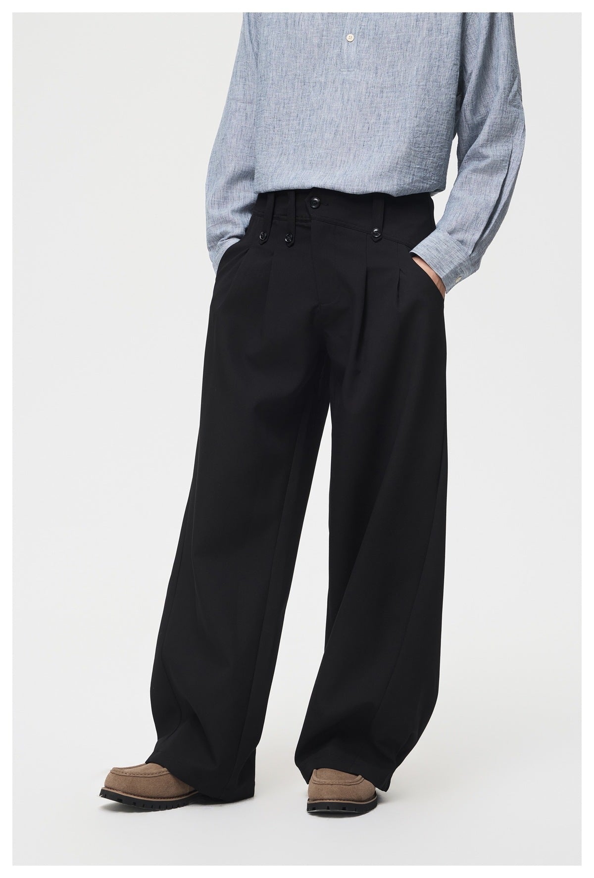 Angled front view of a model wearing black wide-leg trousers with a buttoned, tabbed waistband.