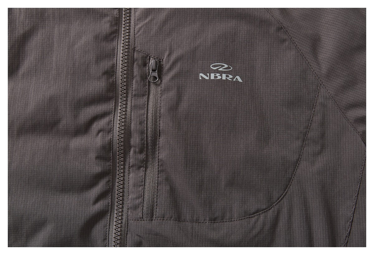 Close-up of a dark charcoal jacket chest with a vertical zip pocket and small light-colored logo.
