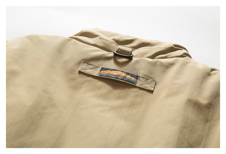 Close-up of a tan jacket back with a small embroidered patch and black D-ring.