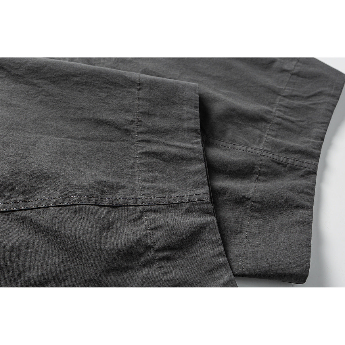 Close-up of charcoal trousers showing a stitched panel seam and hem.