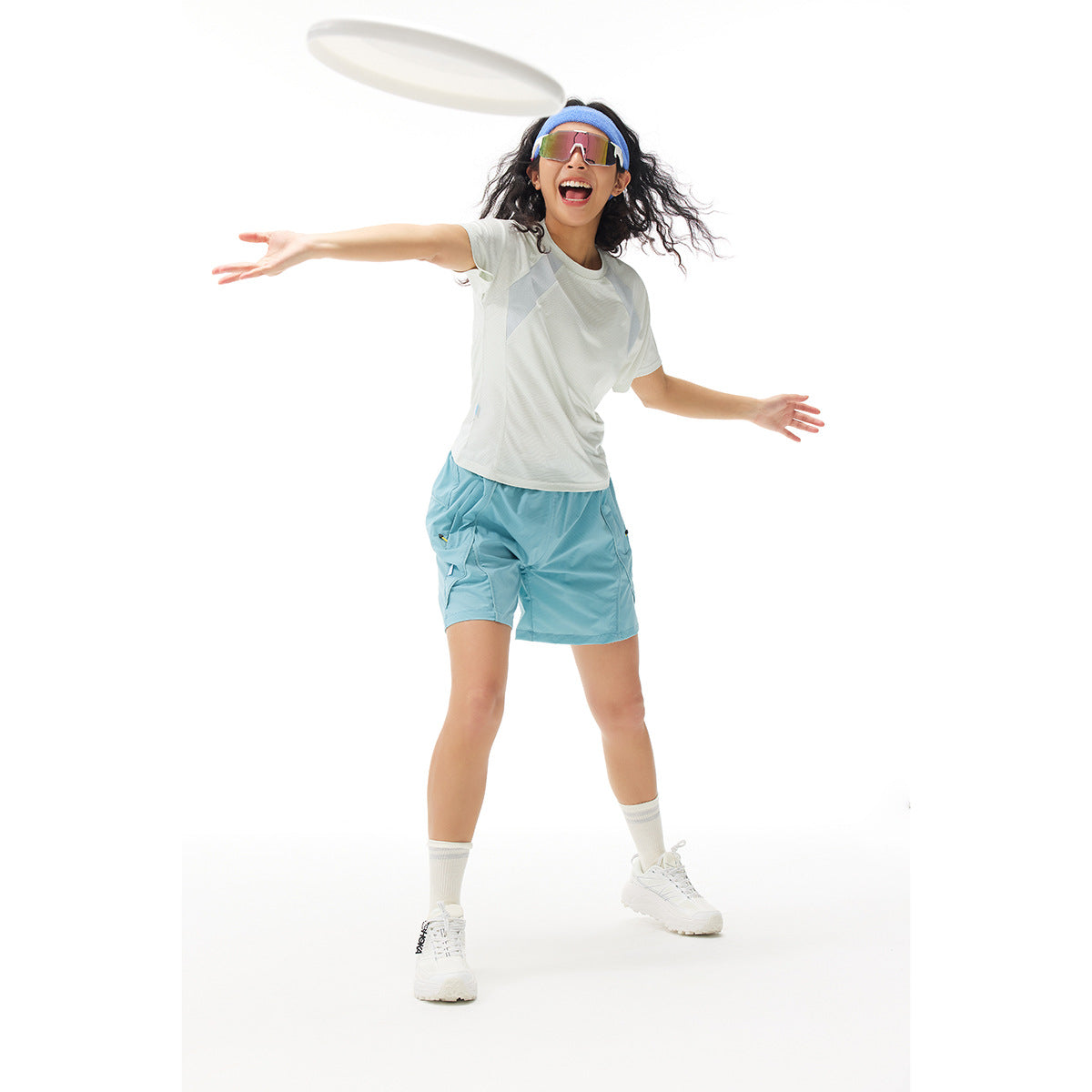 Model playing with a flying disc in a white color-block T-shirt and turquoise shorts.
