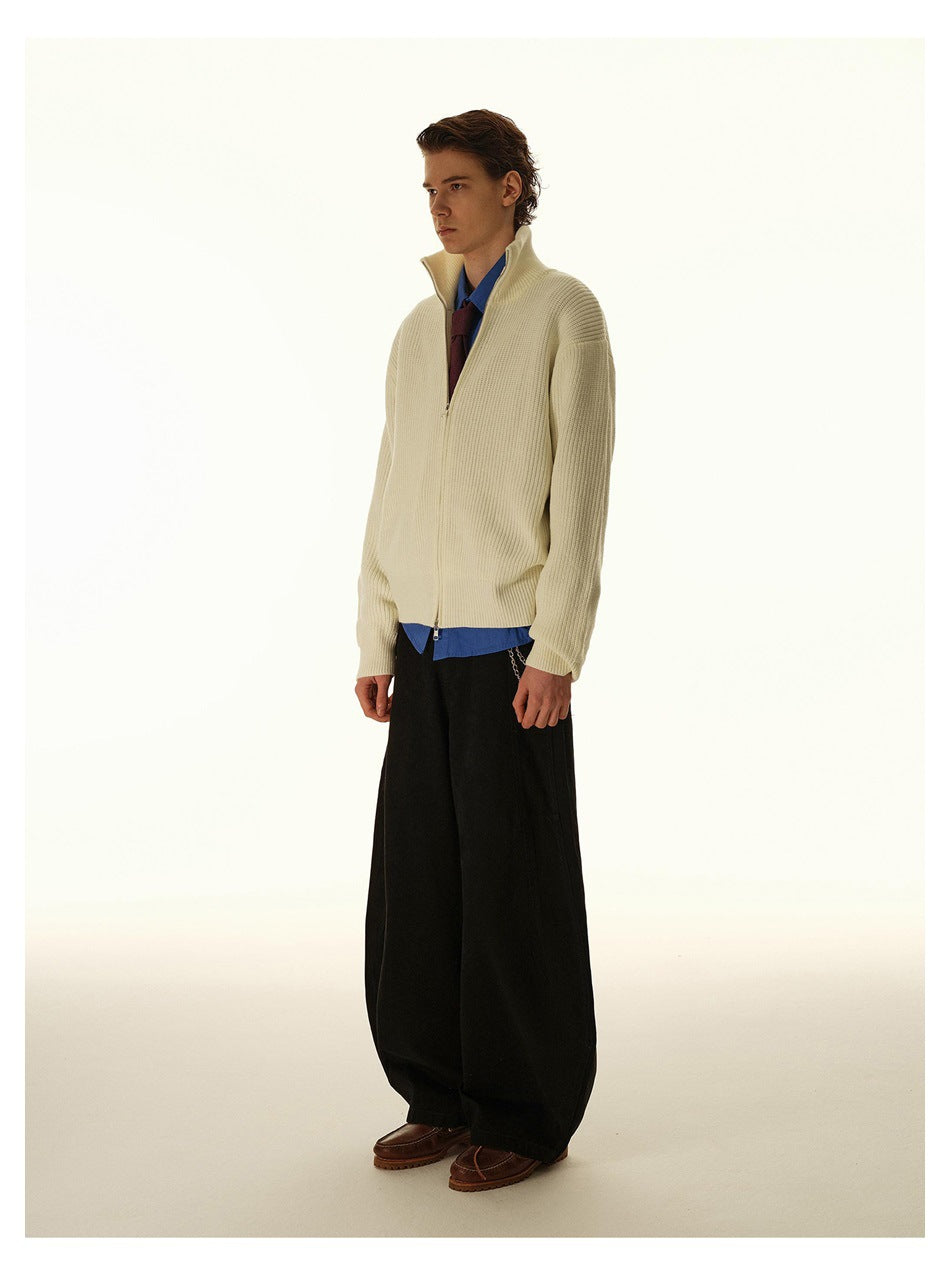Side view of a model wearing a cream ribbed zip-up cardigan with wide black trousers.