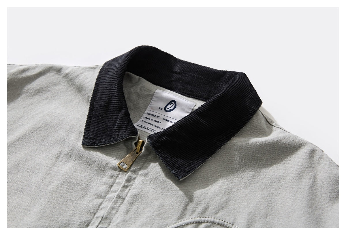 Close-up of a light gray jacket with a black ribbed collar, brass zipper, and visible inner neck label.
