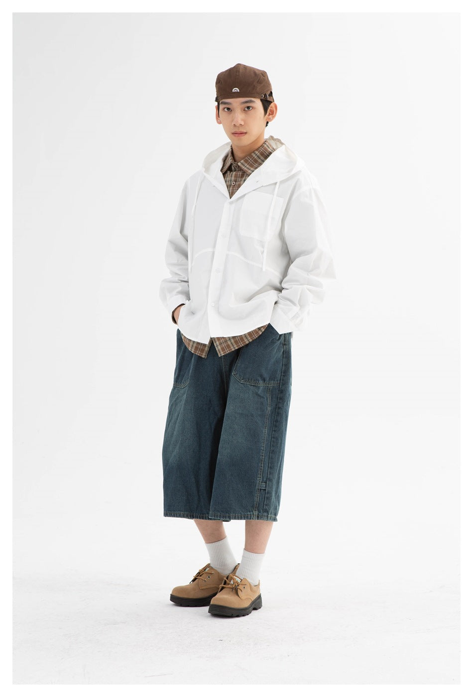 Front view of a model wearing a white hooded button-front jacket, brown plaid shirt and wide dark denim shorts.