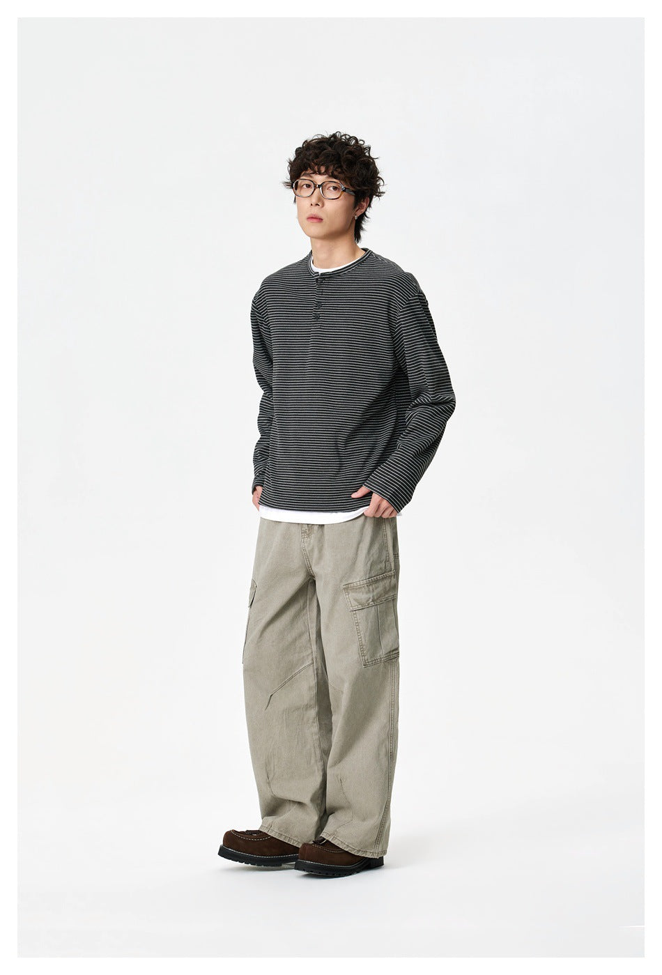 Model wearing a black thin-striped henley with a white layer underneath and loose khaki cargo pants.