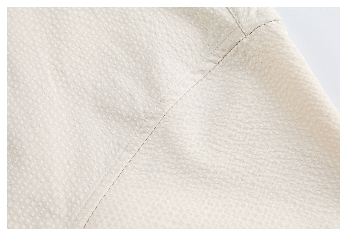Close-up of off-white textured fabric with a curved stitched seam and garment edge.