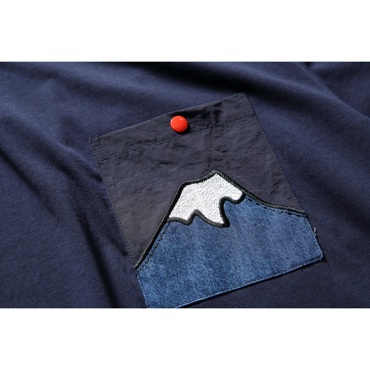 Close-up of a navy T-shirt pocket with a red snap and a blue-and-white mountain appliqué.