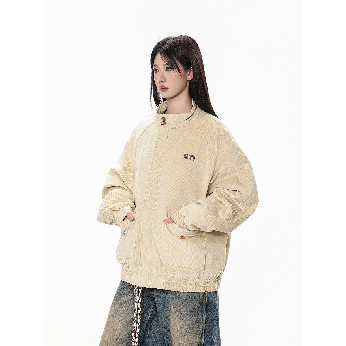 Three-quarter view of a model wearing a beige oversized jacket with a raised collar, snap-front closure, and flap pockets.